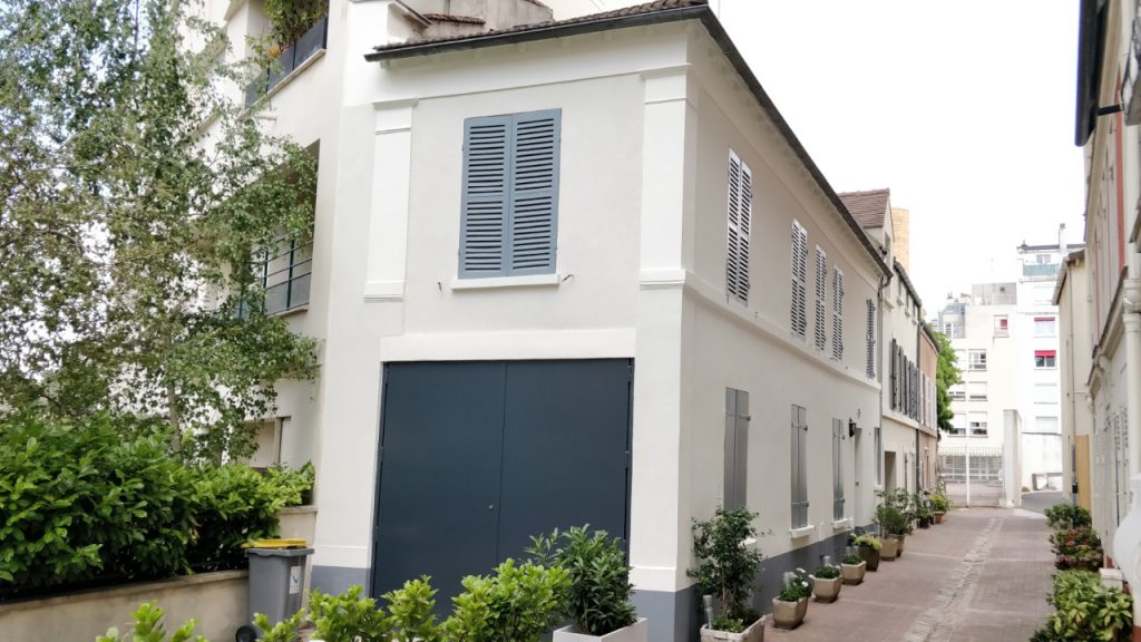 Façade de maison VERTIKAL rénovée avec volets gris et grand portail